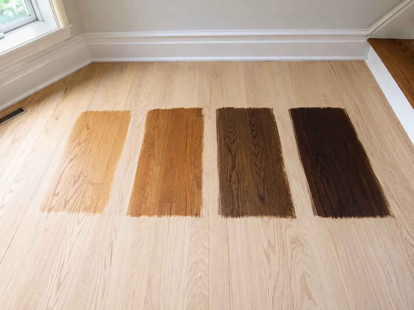 Four stain color samples brushed side by side on a freshly sanded white oak floor in Sarasota
