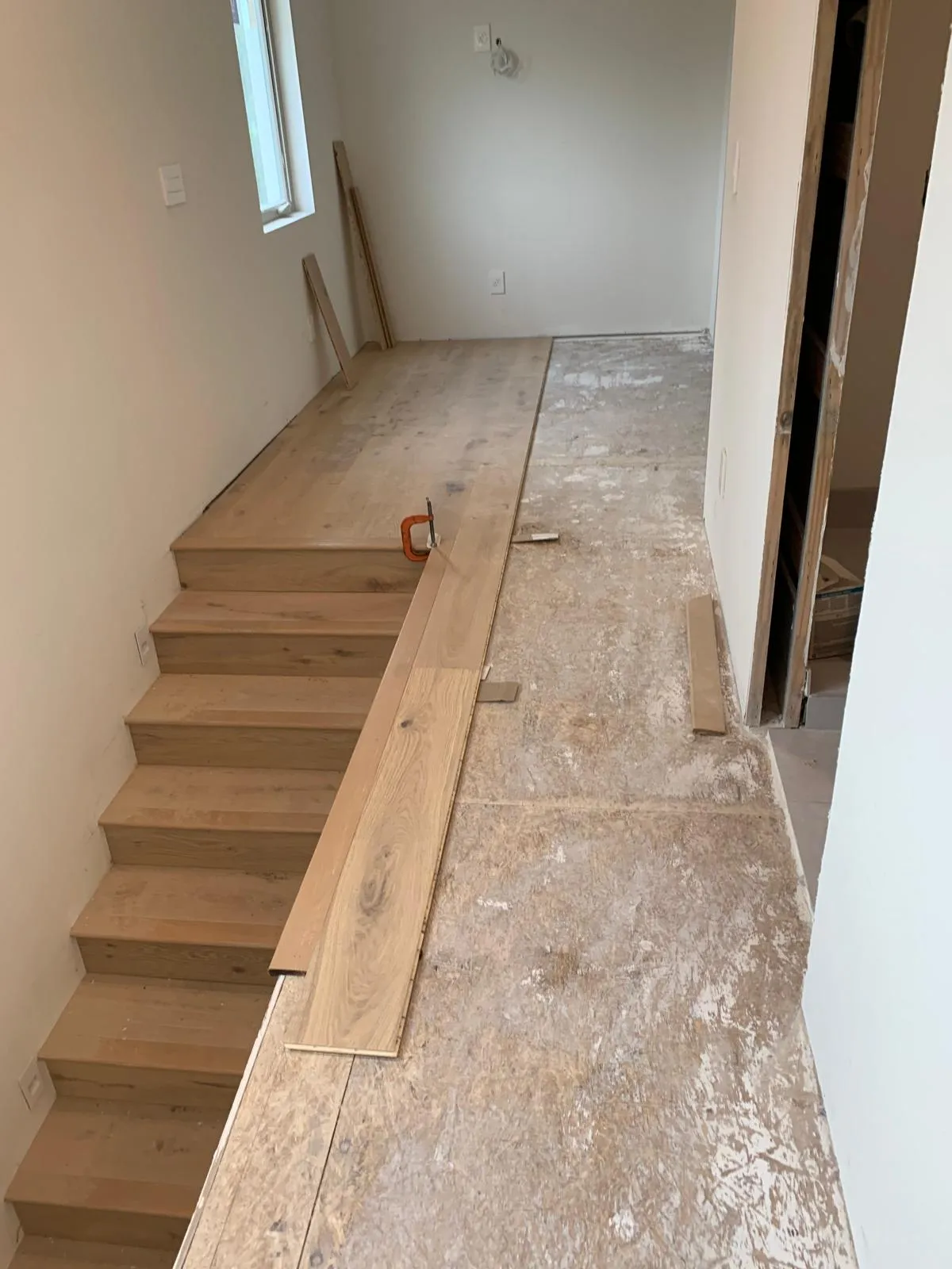 Custom white oak stair treads installed one by one alongside the hallway floor